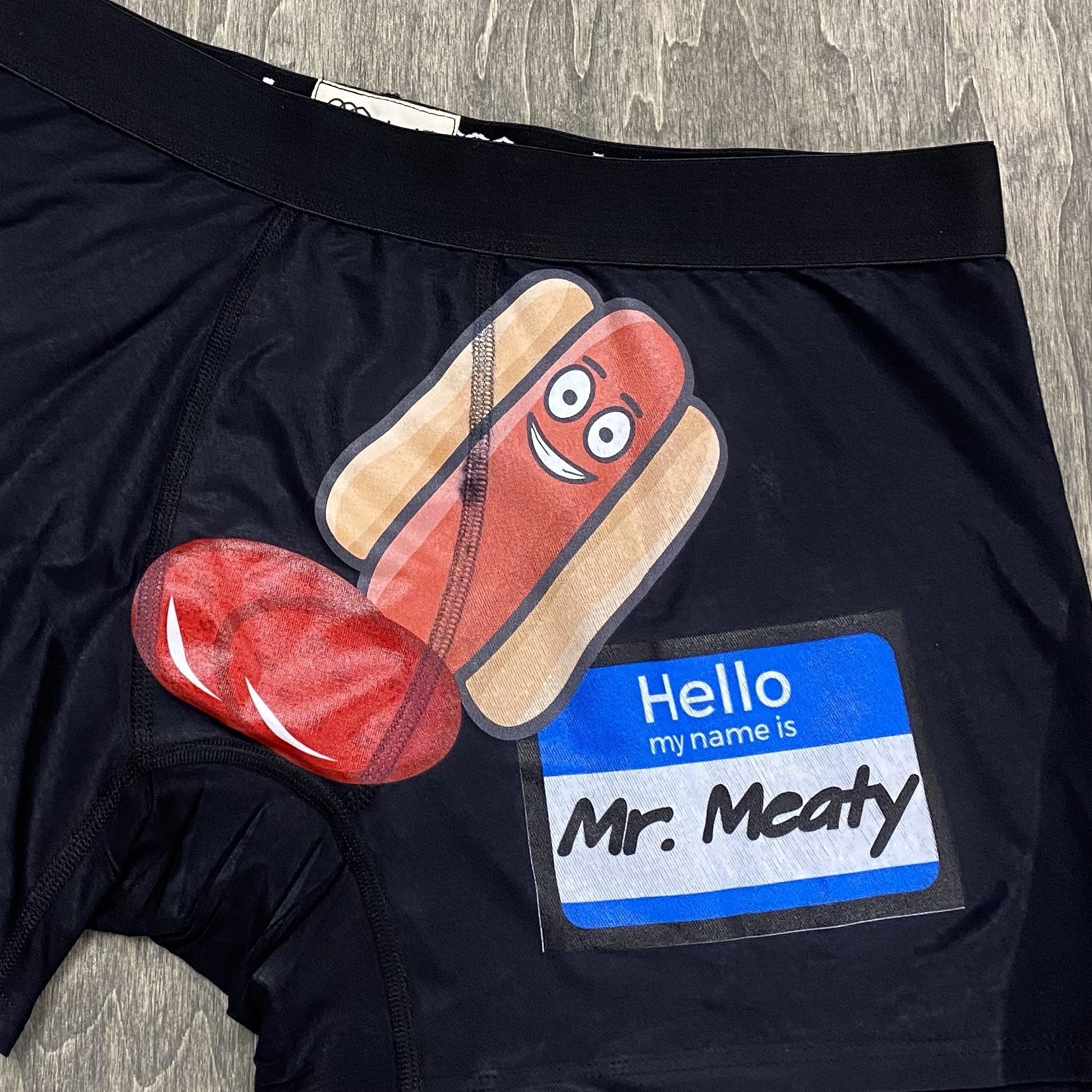 black boxer briefs showing a custom inked design - a hot dog, some salami, and a name tag that says "hello my name is Mr. Meaty" 