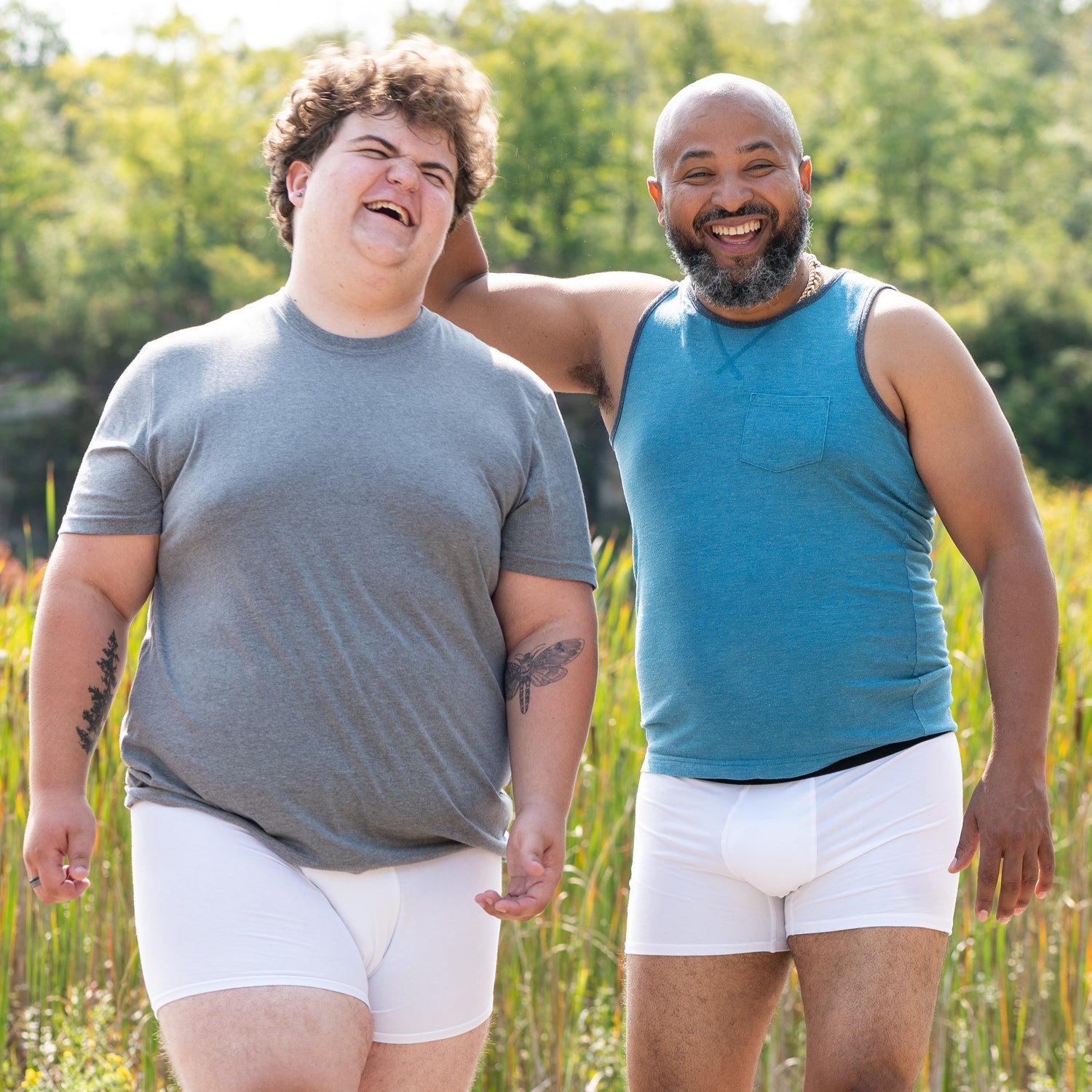 two guys in white do and dare boxer briefs and shirts standing in a field laughing
