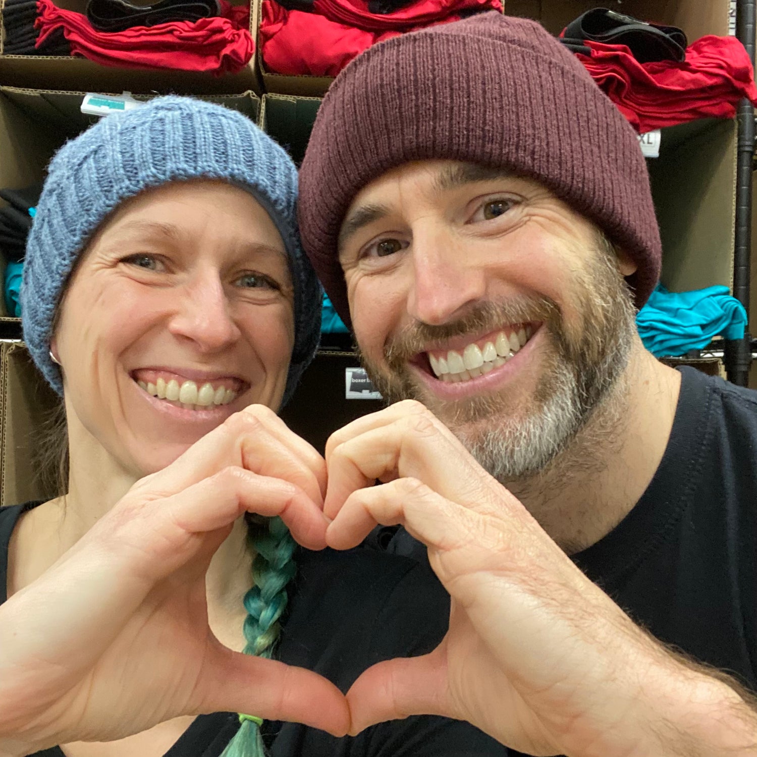 rob and sarah, co-founders of do and dare undie co, smiling and looking at the camera while making a heart with their hands