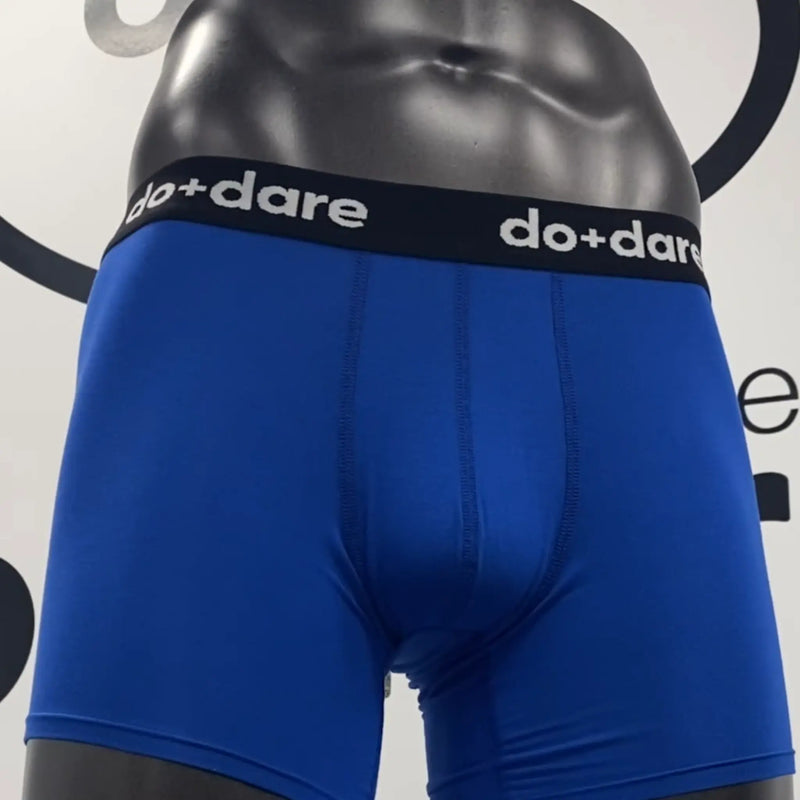 Blue boxer briefs with black waistband featuring 'do+dare' branding on a plain background.
